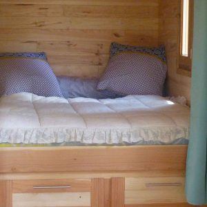 Cabane en bois avec un lit douillet et des coussins colorés. Parfait pour un séjour unique.