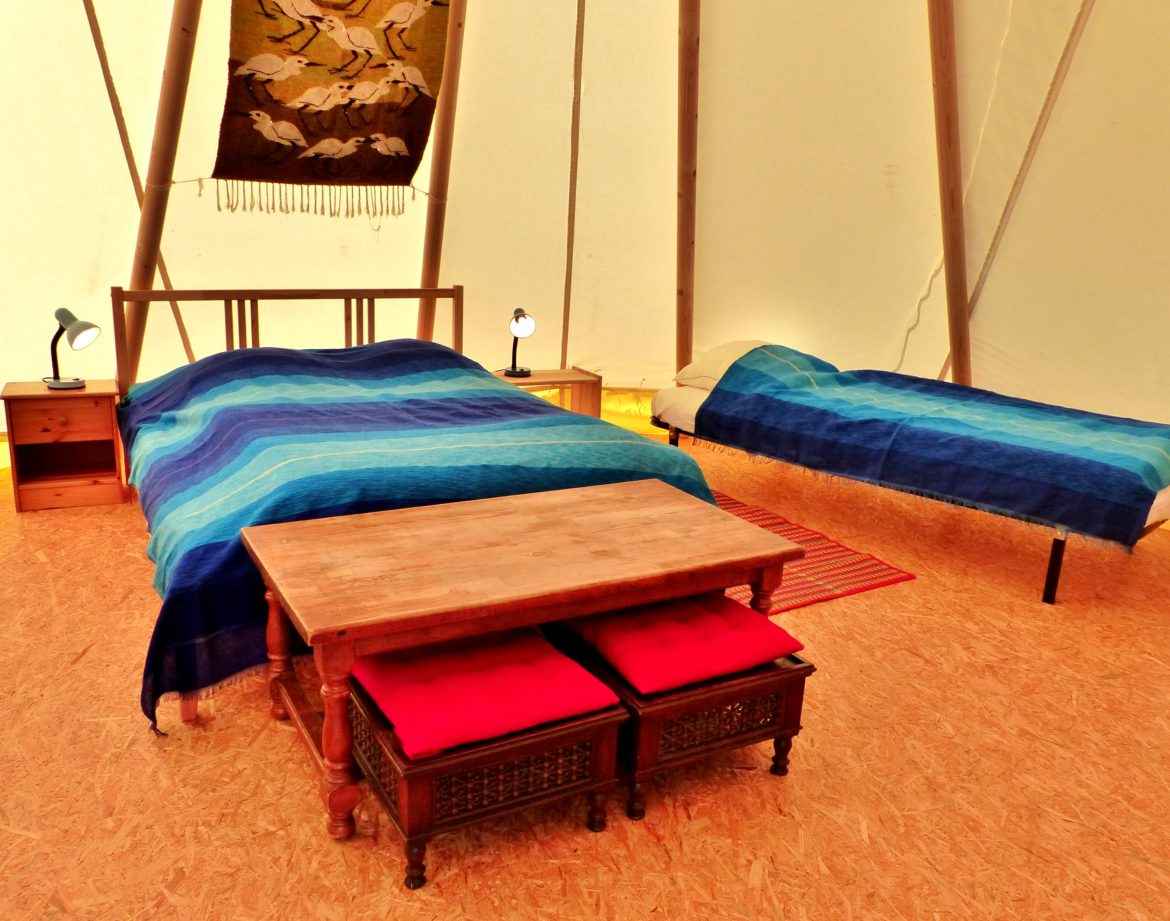 Tente confortable en Auvergne, avec lits aux draps bleus et table en bois.