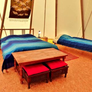 Tente confortable en Auvergne, avec lits aux draps bleus et table en bois.