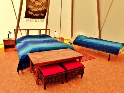 Tente confortable en Auvergne, avec lits aux draps bleus et table en bois.
