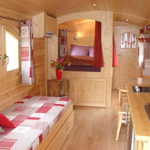 Intérieur chaleureux dune roulotte en bois, lit douillet et décoration rustique.