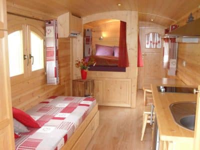 Intérieur chaleureux dune roulotte en bois, lit douillet et décoration rustique.