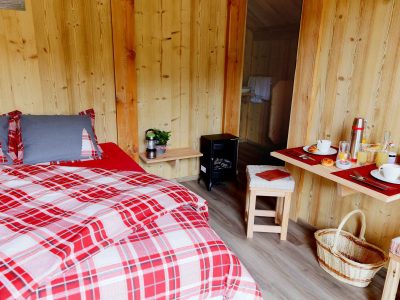 Chalet en bois chaleureux avec lit à carreaux et petit-déjeuner sur table.