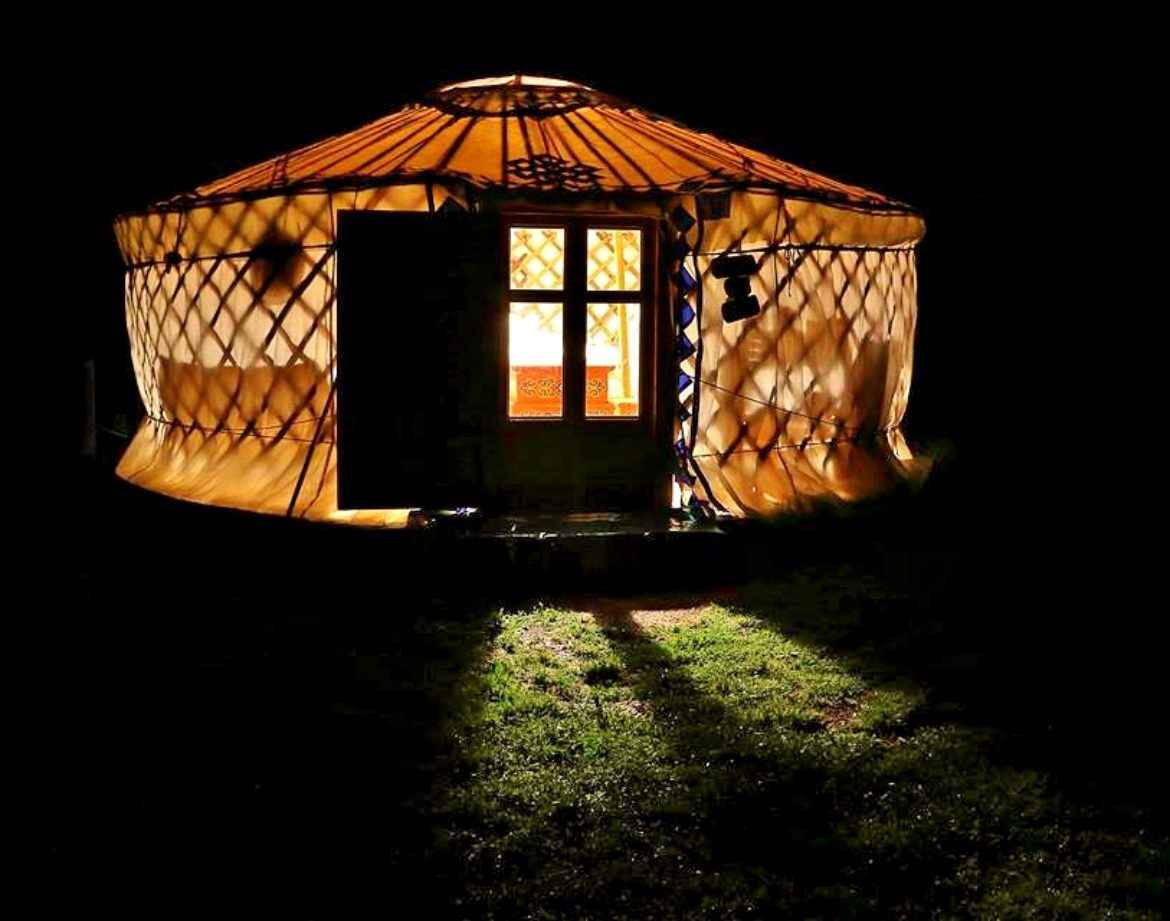 Yourte lumineuse en Auvergne, illuminée la nuit, offrant une ambiance chaleureuse.