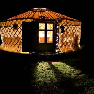 Yourte lumineuse en Auvergne, illuminée la nuit, offrant une ambiance chaleureuse.