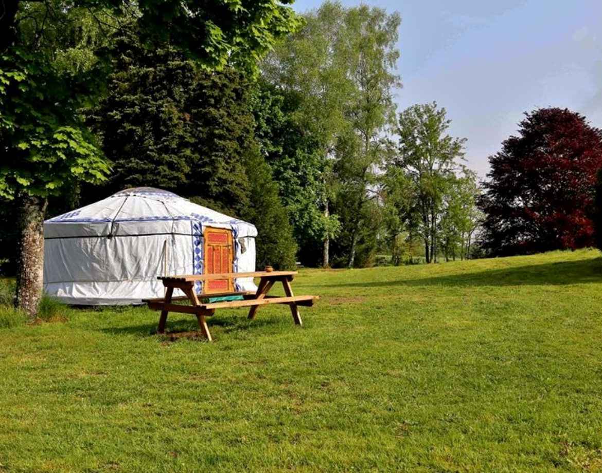 Yourte spacieuse en pleine nature, entourée darbres verdoyants et dune table en bois.