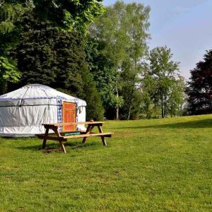 Yourte spacieuse en pleine nature, entourée darbres verdoyants et dune table en bois.