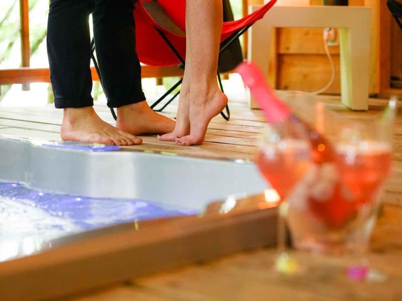 Cabane romantique avec jacuzzi, ambiance chaleureuse et cocktails en arrière-plan.