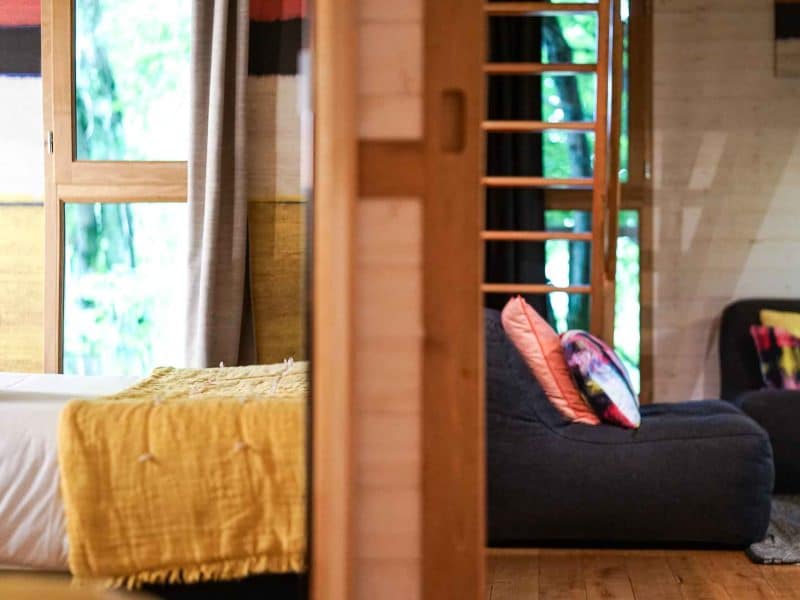 Chalet moderne avec lit douillet et coin salon coloré, entouré de verdure.