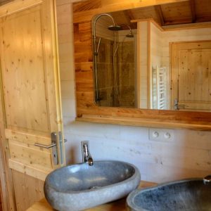 Salle de bain en bois avec vasques en pierre dans un hébergement insolite en Auvergne.