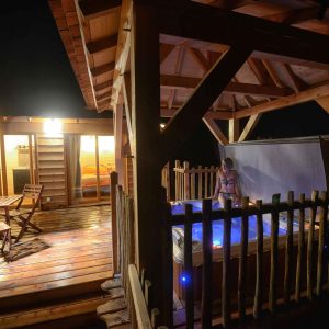 Hébergement insolite en Auvergne : chalet en bois avec jacuzzi extérieur illuminé.