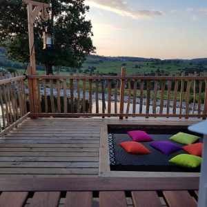 Hébergement insolite en Auvergne : terrasse en bois avec coussins colorés et vue sur la nature.