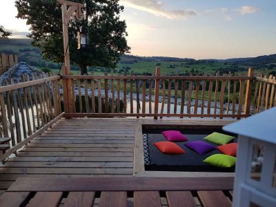 Hébergement insolite en Auvergne : terrasse en bois avec coussins colorés et vue sur la nature.
