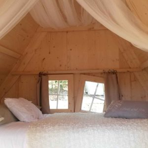 Cabane en bois cosy en Bretagne, avec un lit douillet et des fenêtres lumineuses.