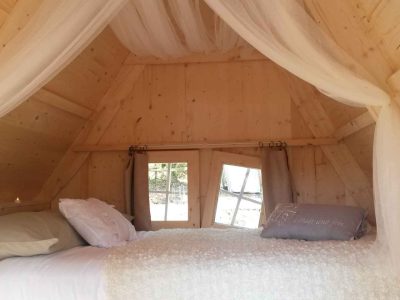 Cabane en bois cosy en Bretagne, avec un lit douillet et des fenêtres lumineuses.