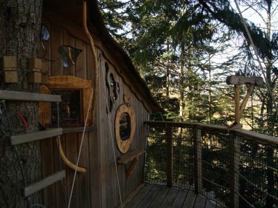 Cabane perchée en bois avec balcon, entourée darbres en Auvergne-Rhône-Alpes.