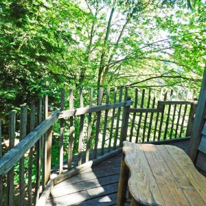 Cabane perchée en bois avec terrasse, entourée darbres verdoyants en Auvergne.