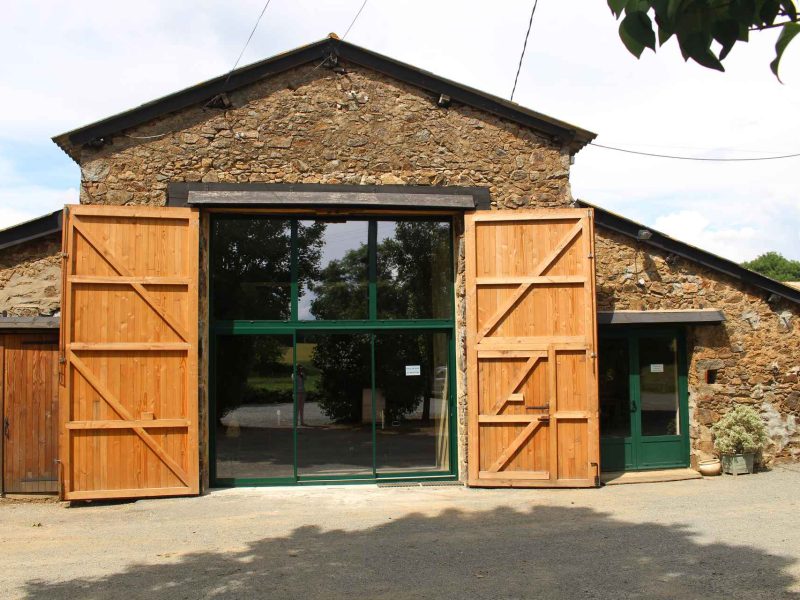 Gîte en pierre avec grandes portes en bois, entouré de verdure. Ambiance rustique et accueillante.