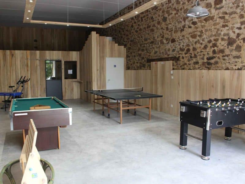 Espace de loisirs dans un gîte, avec billard, ping-pong et décor en bois.