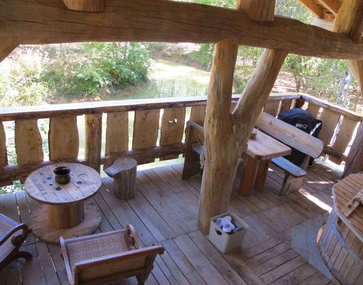 Cabane perchée en bois avec terrasse surplombant un ruisseau paisible.