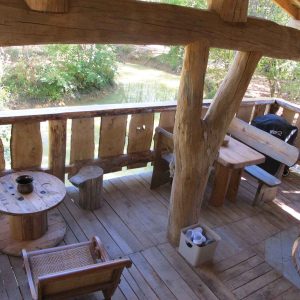 Cabane perchée en bois avec terrasse surplombant un ruisseau paisible.