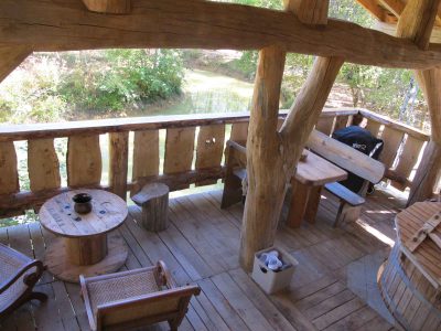 Cabane perchée en bois avec terrasse surplombant un ruisseau paisible.