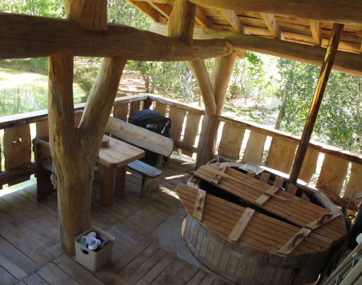 Cabane en bois avec terrasse, baignoire en bois et vue sur la nature environnante.