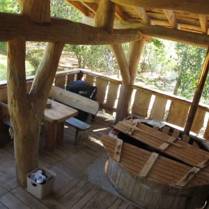 Cabane en bois avec terrasse, baignoire en bois et vue sur la nature environnante.