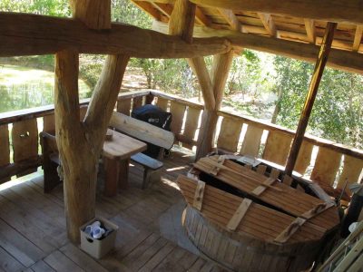 Cabane en bois avec terrasse, baignoire en bois et vue sur la nature environnante.