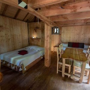 Cabane en bois chaleureuse avec lit douillet et table en bois, ambiance rustique.