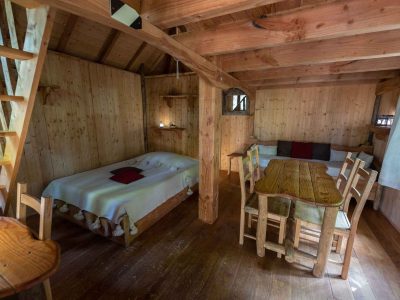Cabane en bois chaleureuse avec lit douillet et table en bois, ambiance rustique.