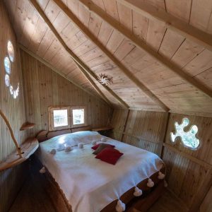 Cabane en bois avec lit douillet et fenêtres rondes, au cœur de lAuvergne-Rhône-Alpes.