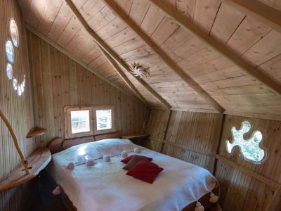 Cabane en bois avec lit douillet et fenêtres rondes, au cœur de lAuvergne-Rhône-Alpes.