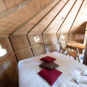 Cabane en bois cosy avec lit douillet et fenêtres originales en Auvergne-Rhône-Alpes.