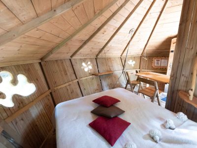 Cabane en bois cosy avec lit douillet et fenêtres originales en Auvergne-Rhône-Alpes.