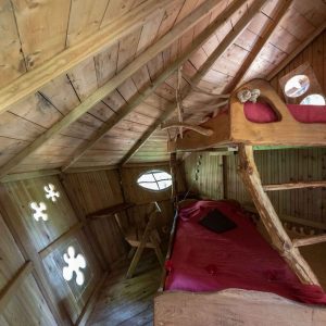 Cabane en bois avec lits en alcôve et fenêtres rondes, ambiance chaleureuse et naturelle.