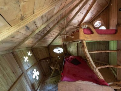 Cabane en bois avec lits en alcôve et fenêtres rondes, ambiance chaleureuse et naturelle.