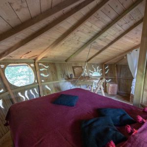 Cabane perchée en bois avec un lit douillet et des coussins colorés.