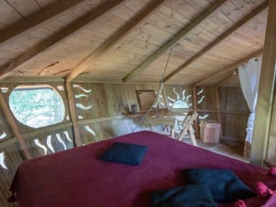 Cabane perchée en bois avec un lit douillet et des coussins colorés.