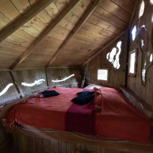 Cabane perchée en bois avec lit douillet et fenêtres originales en Auvergne-Rhône-Alpes.