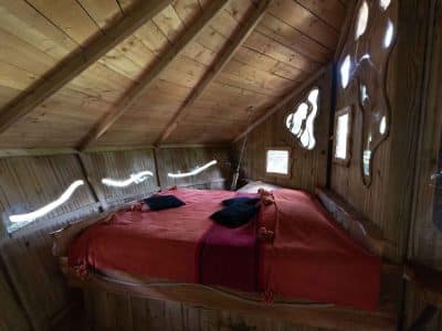 Cabane perchée en bois avec lit douillet et fenêtres originales en Auvergne-Rhône-Alpes.