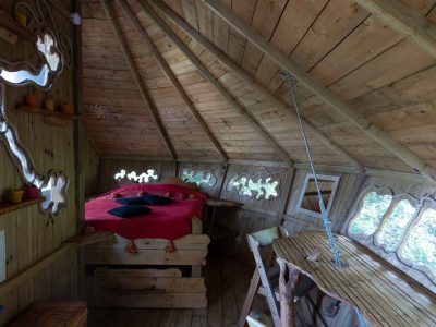 Cabane en bois avec un lit rouge et de grandes fenêtres, offrant une vue sur la nature.