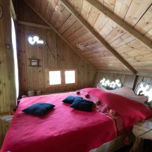Chalet en bois avec lit douillet et coussins noirs, ambiance chaleureuse et naturelle.