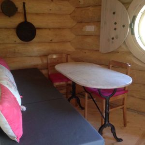 Hébergement insolite en rondins avec table en marbre et fenêtres rondes.