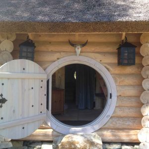 Hébergement insolite en rondins avec une porte ronde et des lanternes suspendues.