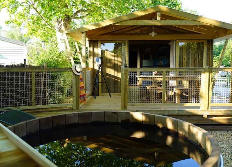 Cabane en bois avec terrasse, entourée de verdure et dun bassin deau.