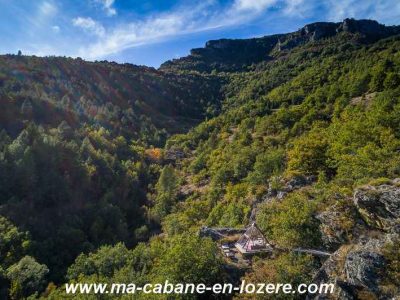 Cabane perchée dans les arbres, entourée de verdure et de montagnes majestueuses.