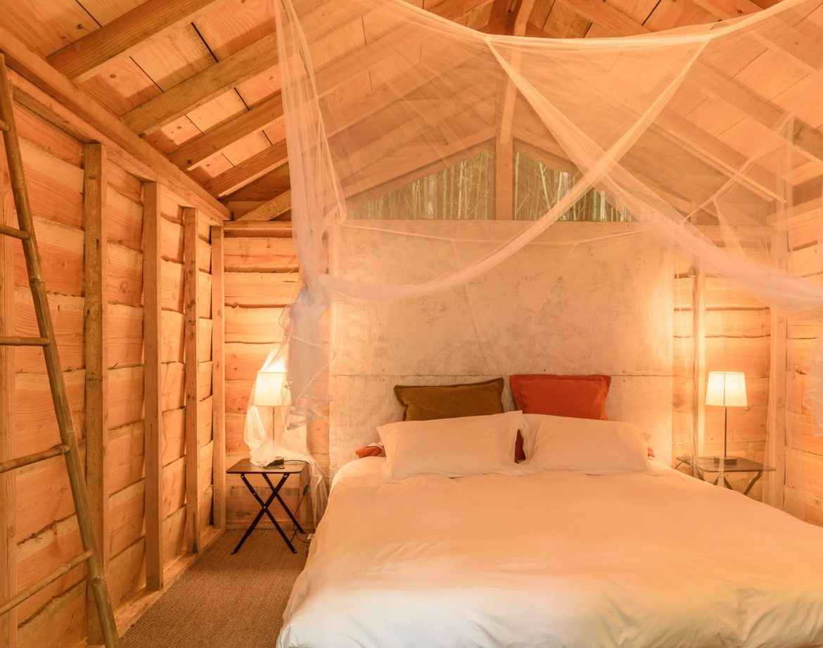 Cabane en bois avec lit douillet, éclairage doux et ambiance chaleureuse.