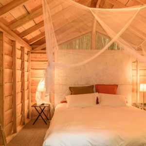 Cabane en bois avec lit douillet, éclairage doux et ambiance chaleureuse.
