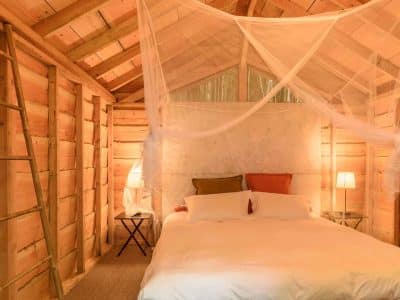 Cabane en bois avec lit douillet, éclairage doux et ambiance chaleureuse.